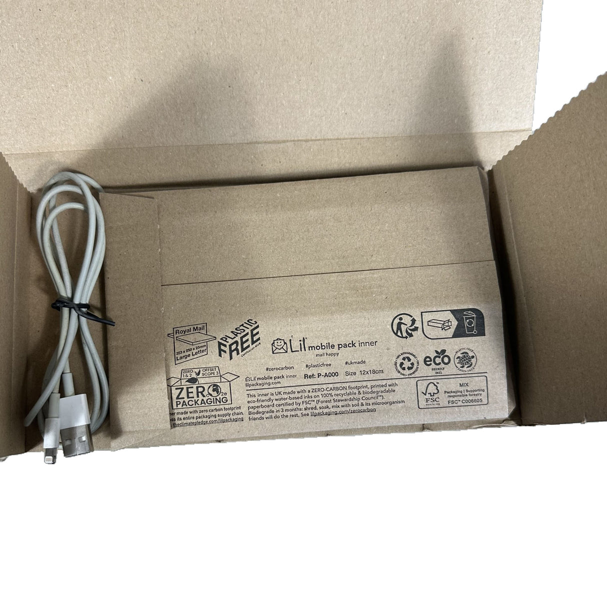 Open cardboard box with a white cable inside, featuring eco-friendly packaging labels.